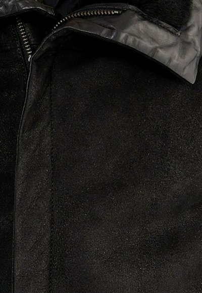 Schwarze Wildlederjacke mit einem Reißverschluss, strukturiertem Kragen und glatter Innenauskleidung; insgesamt matte Oberfläche mit sichtbaren Nähdetails.