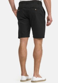 Black cotton shorts with a straight cut, featuring two back pockets and decorative buttons, paired with white slip-on shoes.