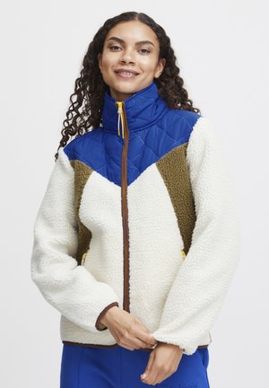 Fleece jacket featuring a cream body, blue quilted upper, and brown accents. Includes a high collar and zippered pockets. Soft texture throughout.