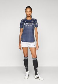 Marinfotbollströja med vita accenter, "Emirates"-logotyp, i kombination med vita shorts, svarta knästrumpor och skor med tre ränder.