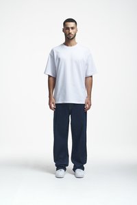 Weißes, übergroßes T-Shirt mit kurzen Ärmeln, kombiniert mit dunkelblauen, weit geschnittenen Jeans und weißen Sneakern, präsentiert vor einem schlichten Hintergrund.