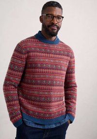 Maglione rosso lavorato a maglia con colletto blu, caratterizzato da intricate trame di fiocchi di neve e forme geometriche. Tessuto texture e caldo.