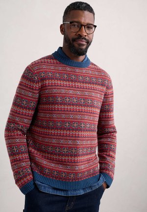 Roter Strickpullover mit blauer Kragen, verziert mit komplizierten Mustern aus Schneeflocken und geometrischen Formen. Strukturierter und warmer Stoff.