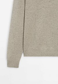 Pull en maille beige à manches longues avec motif tacheté, poignets et ourlet côtelés, présenté de la section médiane au poignet sur fond blanc.