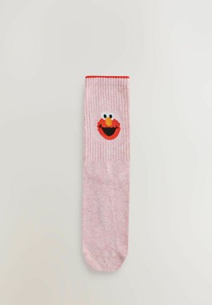 Růžové ponožky s vertikálním žebrováním, po straně s červenou a černou karikaturou obličeje. Manžeta je zvýrazněna červenou barvou.