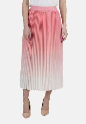 Vrouw in een roze naar wit verlopende geplooide midi-rok, witte top en beige hoge hakken, staand tegen een effen achtergrond.