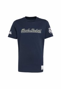Námornícky modré bavlnené tričko s vyšitým nápisom "Real Madrid" v bielej farbe, krátke rukávy s bielym logom Adidas na jednej strane a emblémom klubu na rukáve.