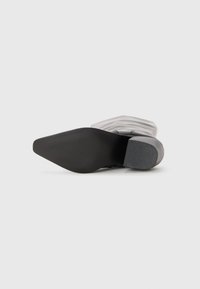 Botte à talons hauts avec une tige en tissu gris, un bout pointu et une semelle en caoutchouc noir texturé. Présente un design plié au niveau de la cheville.