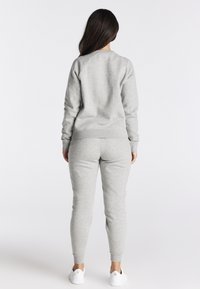 Grijze set van een sweatshirt en joggers gemaakt van zachte stof, met een geribbelde halslijn en manchetten. Draagt witte sneakers.