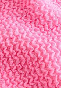 Tekstuirano roza blago z zigzag volančkom, izdelano iz elastičnega materiala z mehkobnim zaključkom.