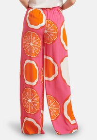 Hose mit weitem Bein aus leuchtend pinkem Stoff, verziert mit großen orangefarbenen und weißen Zitruspflanzmustern. Elastischer Bund für Komfort und einfaches Anziehen.
