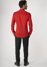 Rode shirt met abstracte zwarte patronen, met knoopsluiting, lange mouwen, gedragen met zwarte broek en schoenen. Plat achteraanzicht.