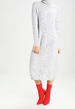 Kobieta ubrana w jasnoszary, długi rękaw, dziany midi sweter z golfem, zestawiona z jaskrawoczerwonymi, szpiczastymi botkami typu sock boots.
