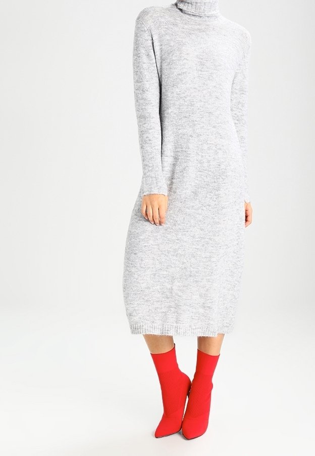 Femme portant une robe midi en maille gris clair à manches longues et col roulé, associée à des bottines chaussettes rouge vif à bout pointu.