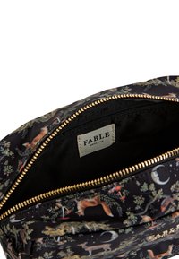 Čierna taška s kvetinovým vzorom a zlatým zipsom. Interiér je vybavený čiernou podšívkou a etiketou s nápisom "FABLE ENGLAND."