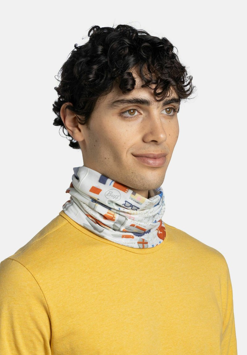 Joven con cabello rizado oscuro lleva un pasamontañas colorido con estampado y una camisa amarilla de manga larga, mirando ligeramente hacia la derecha.