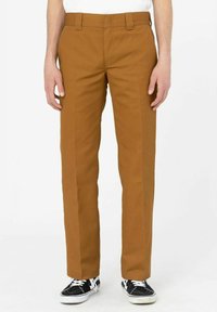 Braune Baumwollhosen mit geraden Beinen, ausgestattet mit Gürtelschlaufen und Seitentaschen, kombiniert mit schwarzen Sneakers mit weißen Akzenten.