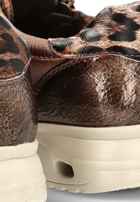 Zapatos de cuero marrón brillante con acentos de tela de estampado de leopardo y suelas gruesas de goma blanca. Se muestran desde ángulos trasero y lateral.