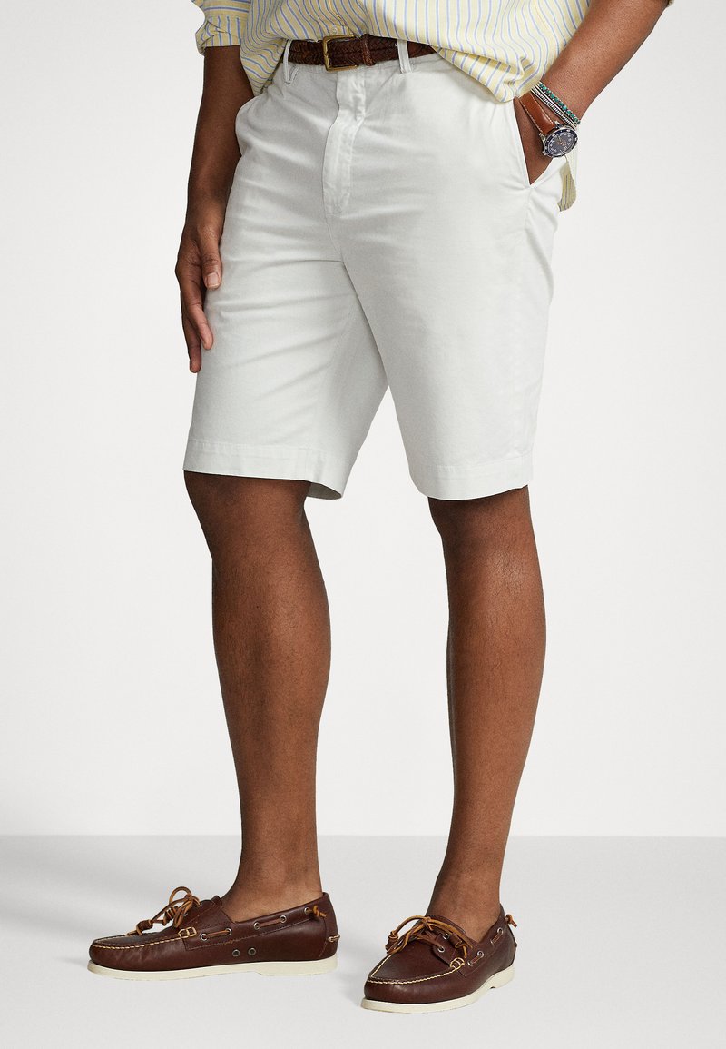 Λευκά σορτς από βαμβακερό μείγμα με επίπεδο μπρο�στινό μέρος, πλάγιες τσέπες και χαλαρή εφαρμογή, συνδυασμένα με καφέ δερμάτινα σκαφτά παπούτσια και υφασμένο ζωνάκι.