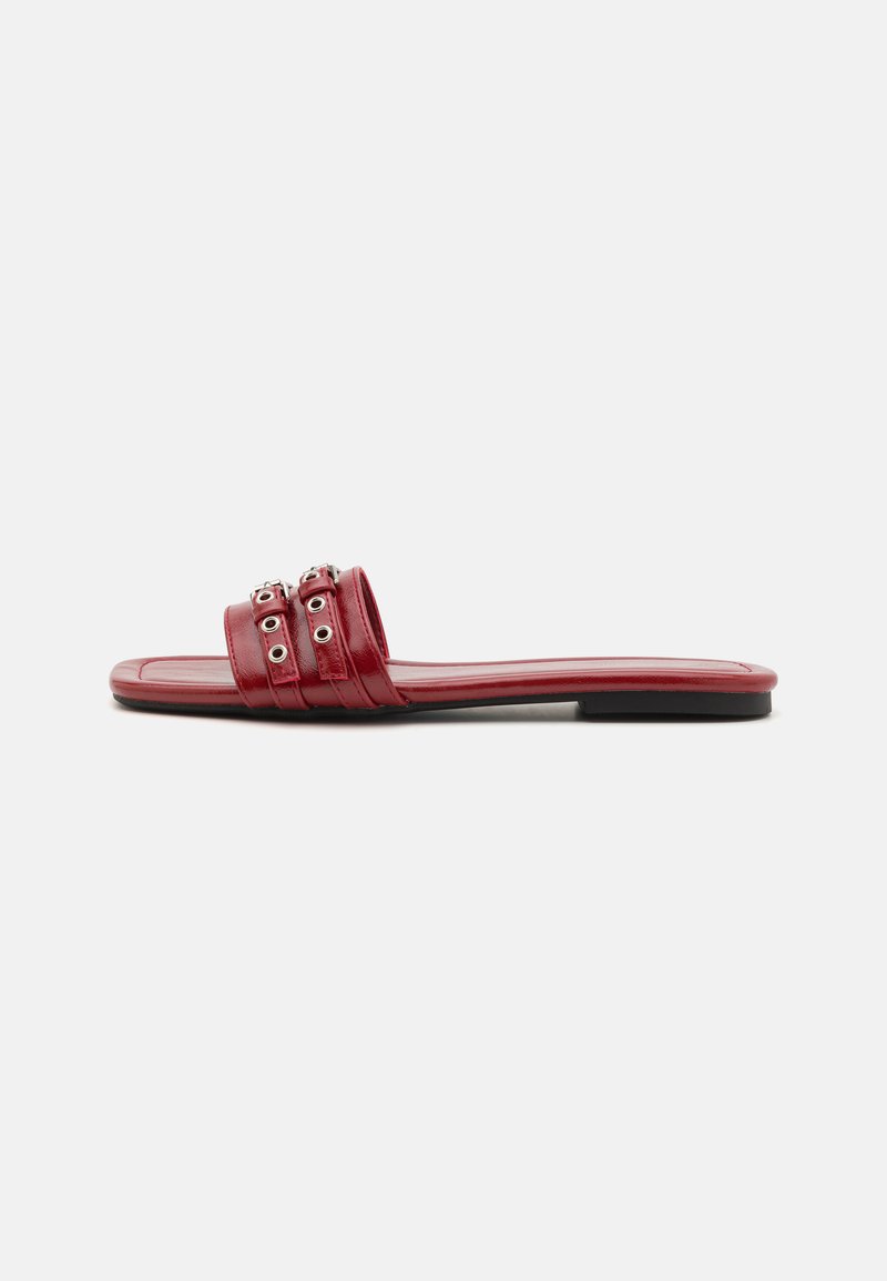 Red leather slide sandals feature two horizontal straps with silver grommets, a flat heel, and a smooth, glossy finish.