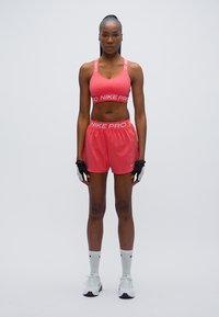 Αθλητικό σουτιέν και σορτς Nike Pro σε φωτεινό ροζ, με έντονο λευκό λογότυπο, συνδυασμένα με λευκές αθλητικές κάλτσες και παπούτσια.