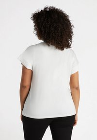 Blusa blanca de manga corta con un corte relajado, textura suave, dobladillo curvado y aberturas en los laterales, combinada con pantalones oscuros.