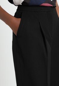 Svarta plisserade byxor med sidofickor, gjorda av ett mjukt tyg. Har en skräddarsydd passform med en hög midja.