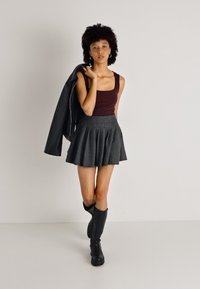 Μπορντό αμάνικο μπλουζάκι συνδυασμένο με φούστα γκρι πλισέ. Το μοντέλο φοράει ψηλές μαύρες μπότες μέχρι το γόνατο και κρατάει μια μαύρη ζακέτα στον ώμο της.