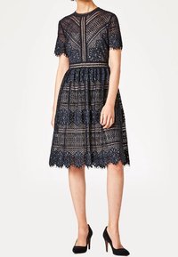 Spitzenkleid in Marineblau, mit kurzen Ärmeln, floralen Mustern, tailliertem Schnitt und einem knielangen Rock mit gewelltem Saum.