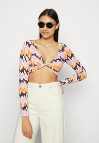 Top cropped de manga longa com um padrão de ondas multicoloridas em rosa, laranja e castanho; combinado com calças brancas de cintura alta.