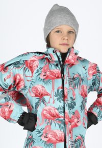 Colorful waterproof jacket featuring a light blue background with pink flamingo prints and green foliage, paired with a grey beanie.