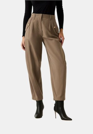 Donna che indossa pantaloni beige a vita alta con pinces e tasche con bottoni, top aderente nero a maniche lunghe e stivali neri con tacco e punta affilata.