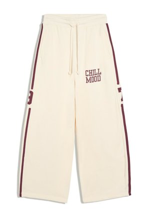 Pantalon de survêtement crème à jambes larges avec bandes latérales bordeaux, poches avant, taille à cordon et texte « "CHILL MOOD" » sur la cuisse gauche.