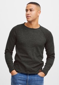 Donkergrijze longsleeve shirt met een ronde hals en raglanmouwen, gemaakt van een gestructureerde stof, gecombineerd met blauwe spijkerbroek.