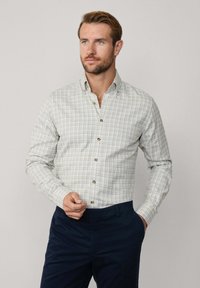 Overhemd met knoopsluiting van lichte stof met een geruit patroon in wit, groen en marineblauw. Heeft een gespitse kraag en bruine knopen.