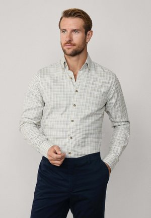 Overhemd met knoopsluiting van lichte stof met een geruit patroon in wit, groen en marineblauw. Heeft een gespitse kraag en bruine knopen.