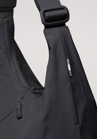 Borsa a spalla in nylon nero con forma arrotondata, tracolla regolabile, chiusura con cerniera e una piccola etichetta grigia accentuata sul lato.