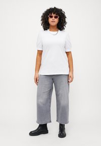 White short-sleeve t-shirt with puff sleeves, paired with wide-leg gray jeans and black ankle boots. Accessorized with pink sunglasses.