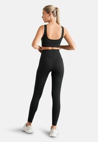 Crni sportski crop top i tajice visokog struka napravljene od glatkog, rastezljivog materijala, s jednostavnim dizajnom bez istaknutih uzoraka.