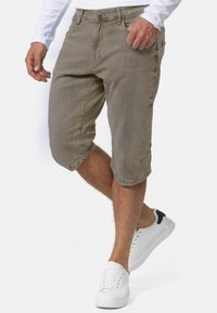 Knælange beige shorts lavet af tekstureret stof med frontknaplukning, sidelommer og opkrøllet kant, båret med hvide sneakers.