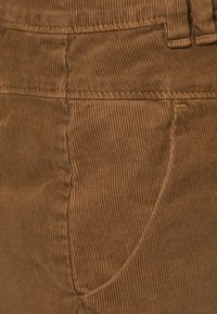 Gros plan d’un tissu en velours côtelé marron avec une couture visible de poche et un passants de ceinture sur un vêtement.