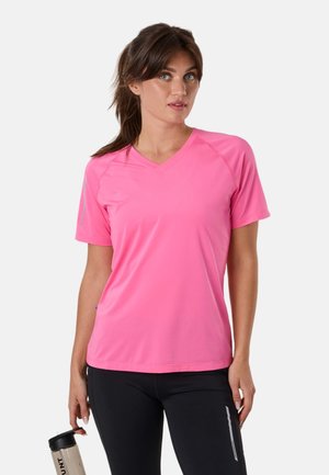 Femme aux cheveux bruns attachés en queue de cheval, portant un t-shirt de sport rose à col en V et un legging noir, tenant une bouteille d'eau beige dans la main gauche.