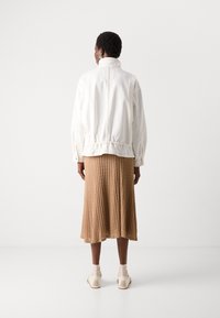 White bomber jacket with cuffed sleeves, paired with a beige pleated midi skirt. The outfit is complemented by white shoes and beige socks.