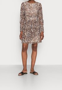 Robe à imprimé léopard avec manches longues, tissu transparent, taille cintrée et coupe mi-genou. Associée à des sandales plates noires.