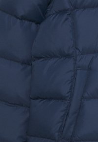 Giacca puffa invernale blu navy con un design trapuntato, caratterizzata da sezioni imbottite testurizzate e una tasca laterale. Finitura in tessuto liscia.