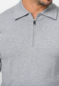 Grau zip-up Pullover mit strukturiertem Stoff, ausgestattet mit einem flachen Kragen und einem kontrastierenden Reißverschluss. Nahtdetails sorgen für visuelles Interesse.