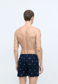 Mørkeblå badebukser med elastisk talje, prydet med et mønster af farverige ikoner. Stoffet har en glat overflade.