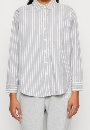 Knopfhemd mit langen Ärmeln in vertikalen grauen und weißen Streifen, Brusttasche vorne, kombiniert mit hellgrauen Jogginghosen mit weißem Schriftzug.