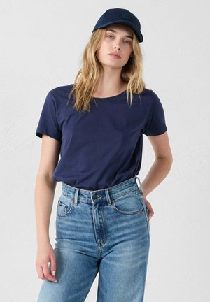 Maglietta in cotone blu marina a maniche corte abbinata a jeans in denim azzurro a vita alta. Vestibilità casual con scollatura rotonda.