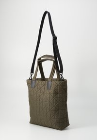 Geknoopte tote bag in olivegroen, met een geometrisch patroon, dubbele handgrepen bovenaan en een verstelbare zwarte schouderband. Soepele textuur en rechthoekige vorm.
